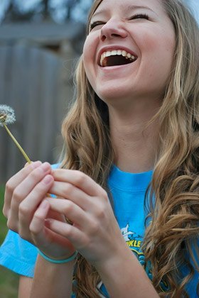 Samantha Alison Thomas laughing, holding a dandelion